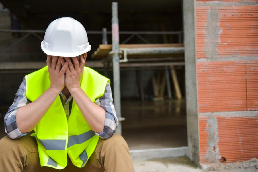 Il lavoratore stanco frustrato con il casco e la maglia di sicurezza bianchi colpisce le sue mani davanti al fronte